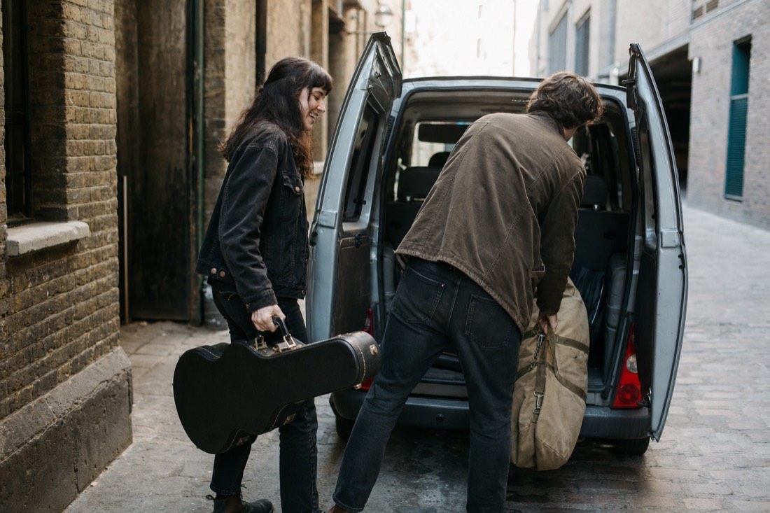 Two musicians loading a guitar case into a small van