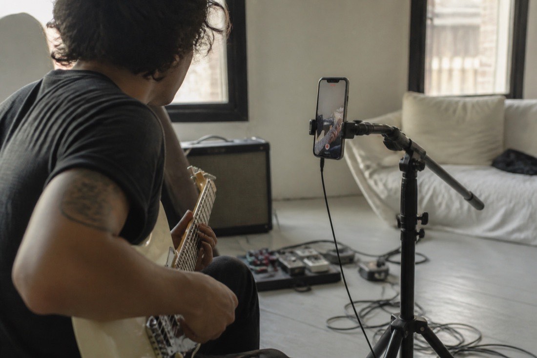 A musician filming a vertical phone video of their hands playing guitar